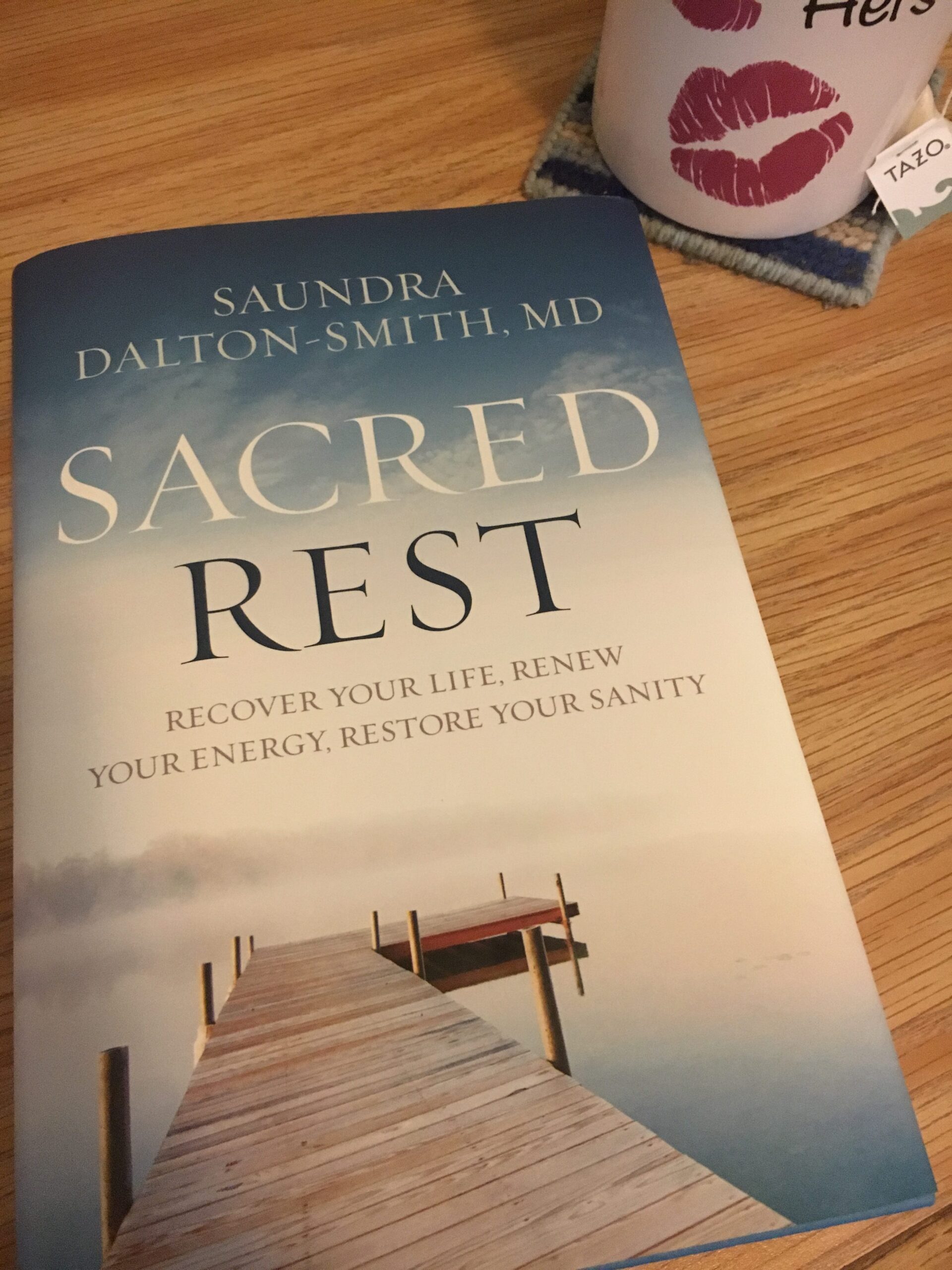 Sacred Rest by Saundra Dalton-Smith, MD book cover with a white mug - decorated with lip prints and the word "hers" - slightly visible in the top right corner and a tea bag with the brand "Tazo" dangling from it