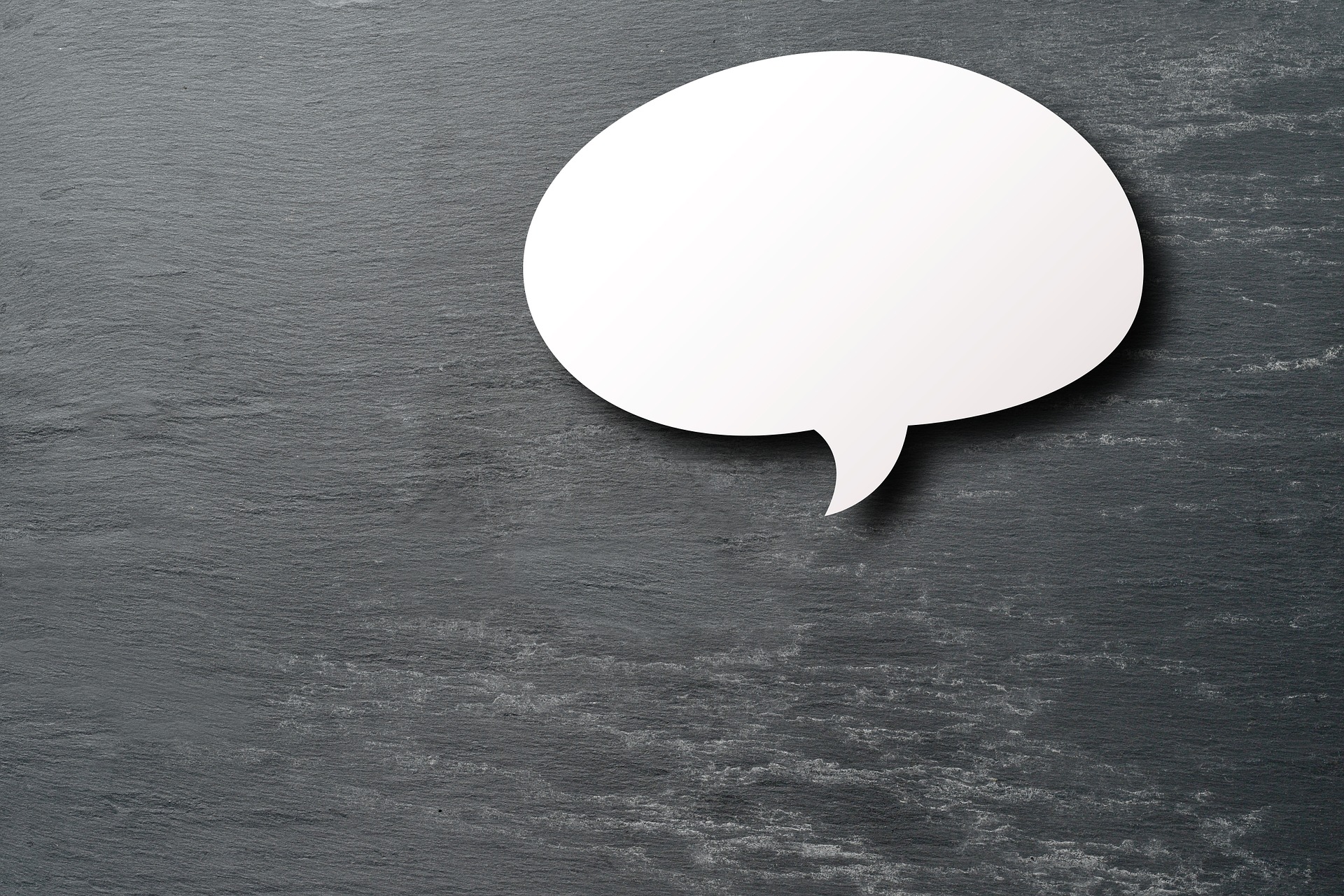 a dark grey-ish wooden surface with a white paper-looking chat box cut out resting on it