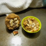 Banana Nut Muffins, one in a yellow silicone cup with a white dish towel with a pale blue stripe on the right side