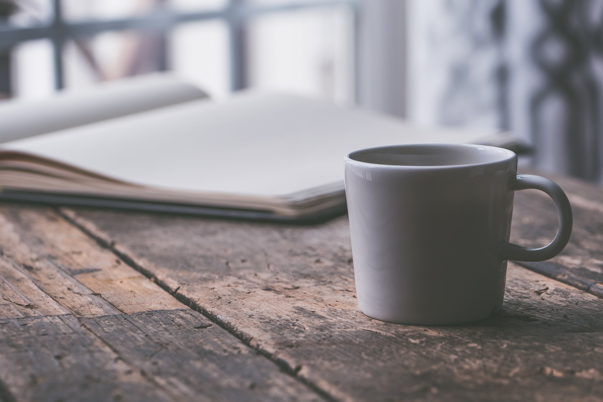 an open notebook on a wooden board surface with a basic light colored mug in the forefront