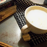 Vanilla Chai Tea Latte in a short white mug on a black and white checkered cloth with a BIGELOW brand box of tea in the top left corner and a cinnamon stick in the bottom left corner