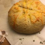 Garlic Cheddar Chive Sourdough bread whole and uncut with a few chives and a partial bulb of garlic sitting in front