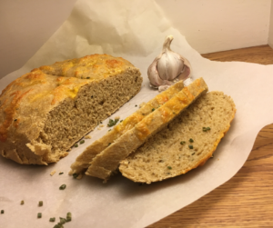 Garlic Cheddar Chive Sourdough Bread sliced on parchment paper, chives scattered across, with a partial bulb of garlic in the background