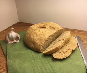 Garlic Parmesan Sourdough Bread sliced with a bread knife on one side and a partial garlic bulb on the other, a green placemat under the bread