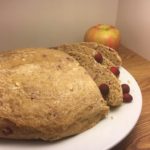 Cranberry Apple Sourdough Bread sliced on a white plate with cranberries scattered and an apple in the background