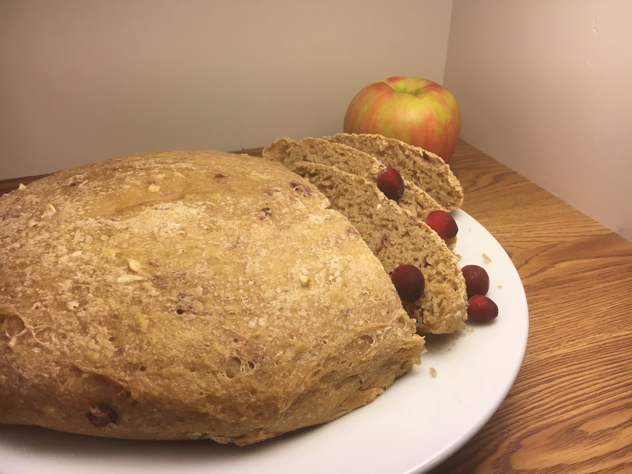 Cranberry Apple Sourdough Bread sliced on a white plate with cranberries scattered and an apple in the background