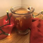 Refined Sugar-Free Mulled Apple Cider in a clear glass handled mug with a red cloth behind and gold Christmas lights lighting the scene