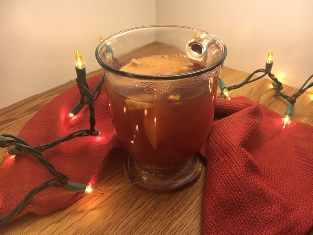 Refined Sugar-Free Mulled Apple Cider in a clear glass handled mug with a red cloth behind and gold Christmas lights lighting the scene