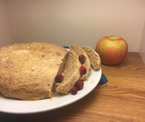 Cranberry Apple Sourdough Bread sliced on a white plate with cranberries scattered across the slices and a whole red and green apple in the background