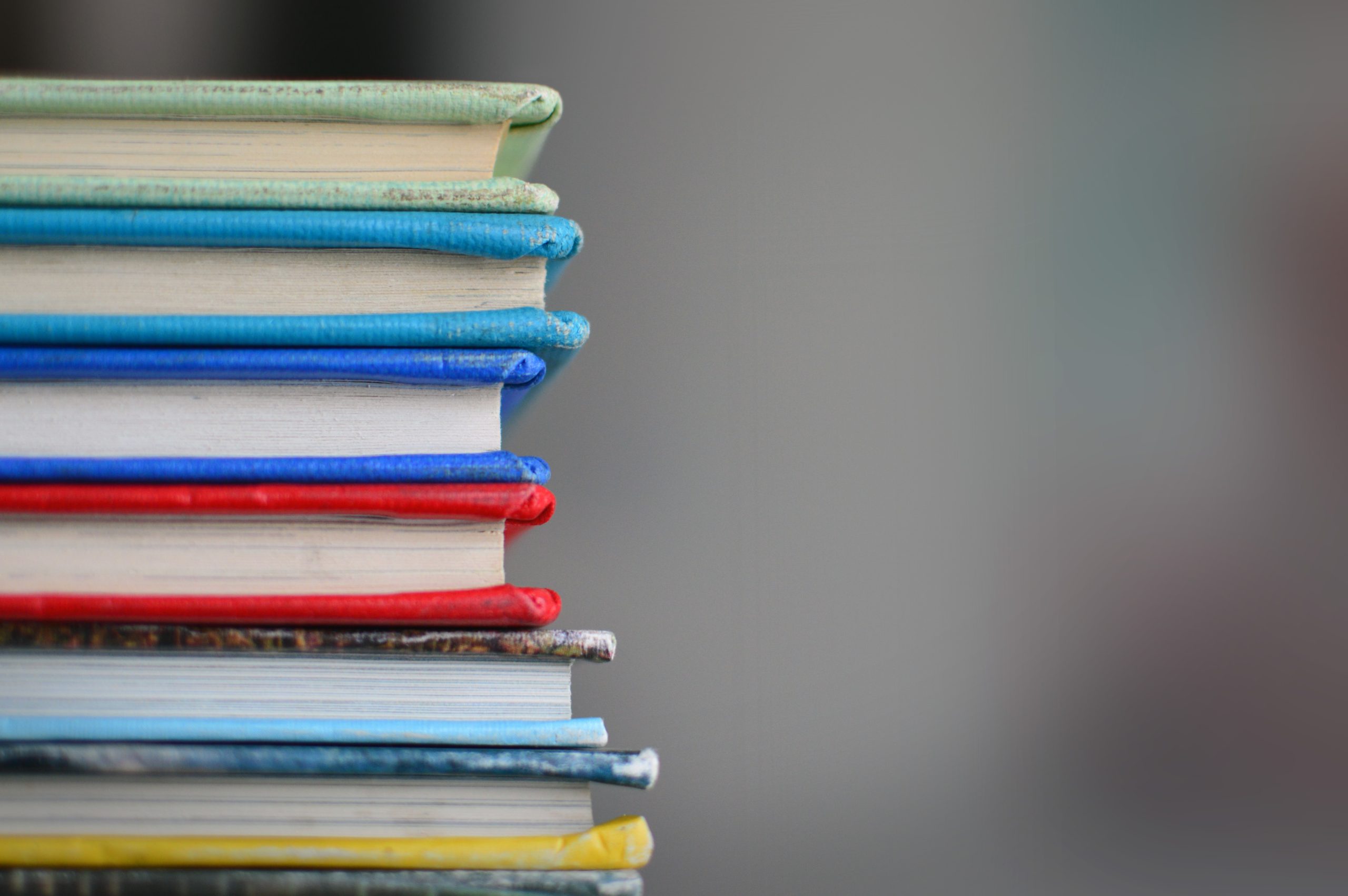 A stack of various colors of books to the left of the image with a blurry, unidentifiable right side