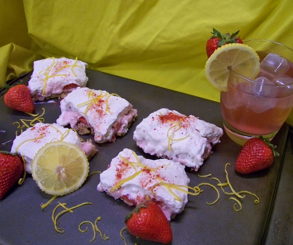 Strawberry Lemonade Bars sliced on a cookie sheet with a glass of lemonade to the back right with whole strawberries around the bars