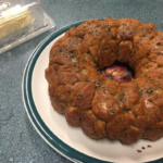 Sourdough Cilantro Lime Monkey Bread in a ring shape on a large plate with a glass butter keeper to the back left of the image