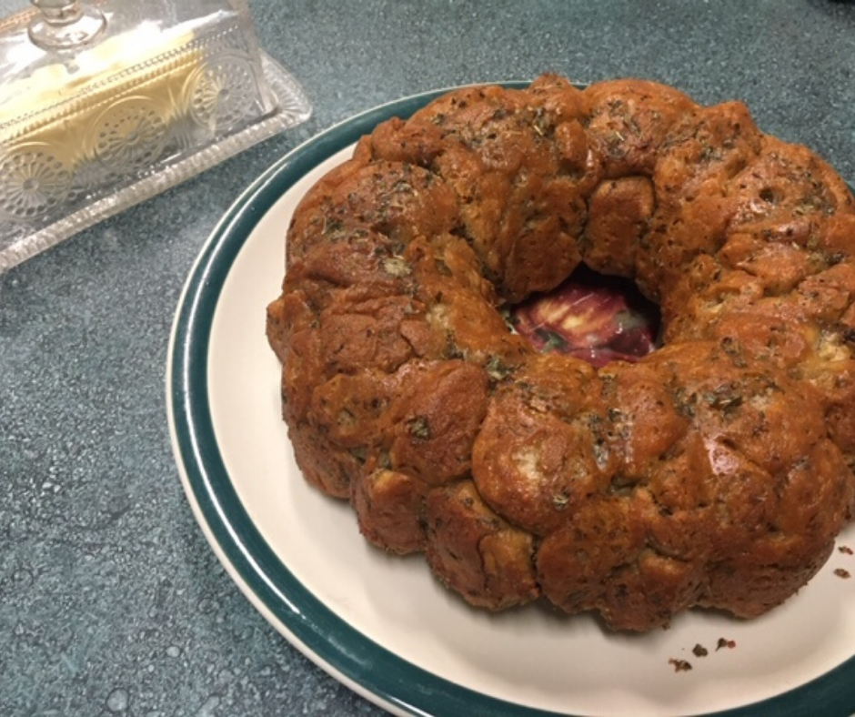 Sourdough Cilantro Lime Monkey Bread in a ring shape on a large plate with a glass butter keeper to the back left of the image