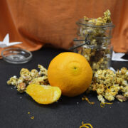 Orange Vanilla Granola spilling out of an antique mason jar, an orange fruit in the front and an orange cloth in the background