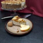 Autumn Apple Cheesecake on a platter with a slice on a plate and a server between