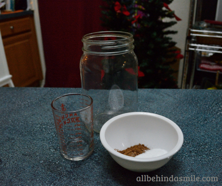 A small plastic white bowl of cocoa powder and sweetener beside a glass measuring cup and large mason jar on blue countertop