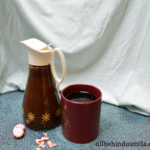 An antique syrup bottle full of peppermint mocha syrup beside a reddish coffee mug