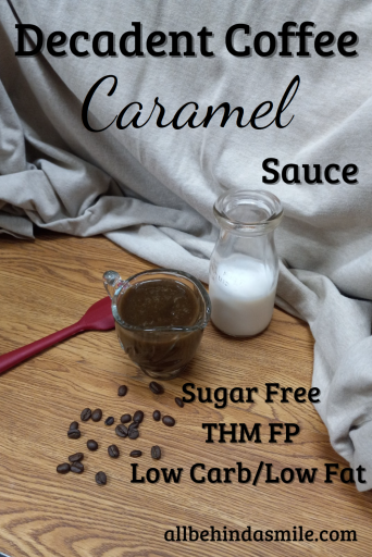 A red spatula on a wooden surface with a container of almond milk behind a small glass dish of coffee caramel sauce, coffee beans scattered in front with text Decadent Coffee Caramel Sauce Sugar free, THM FP, low carb/low fat
