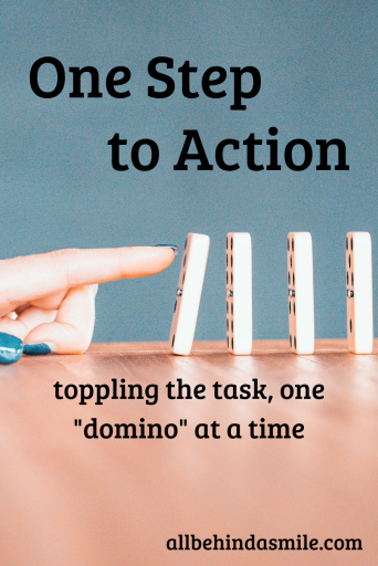 Grey blue background with a wooden table and dominoes upright poised to topple with a finger slightly tipping the first domino to knock them over with the text One Step to Action toppling the task one "domino" at a time