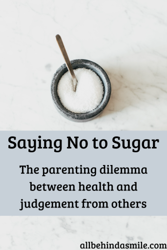 Bowl of sugar with metal utensil in it over light marble background with the text Saying No to Sugar: the parenting dilemma between health and judgement from others