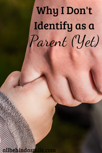 Small child's hand holding the finger of a larger adult hand with the text Why I Don't Identify as a Parent (Yet)